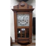 A stained wood cased small wall clock with visible pendulum and eight day striking movement