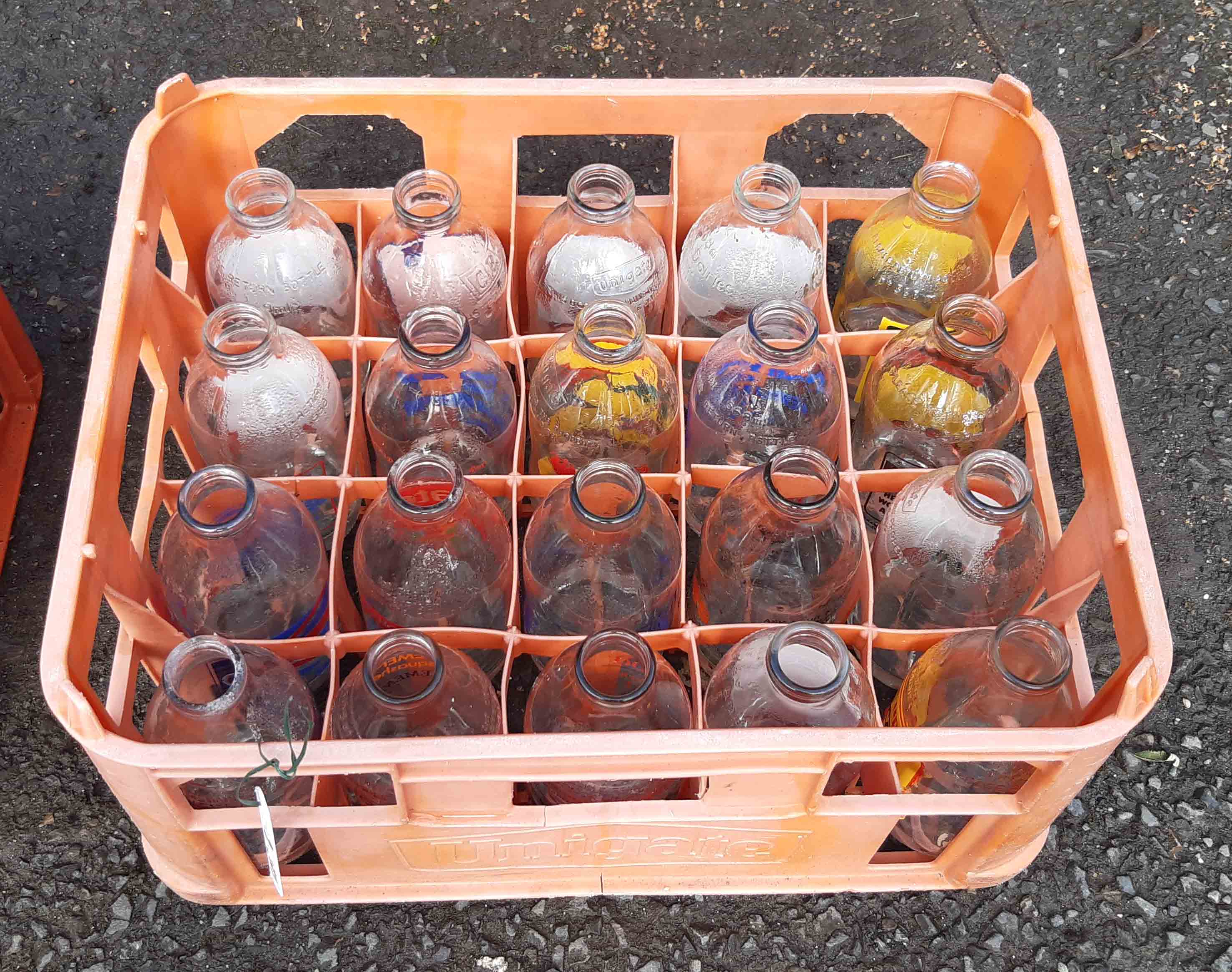 A vintage Unigate plastic milk crate containing twenty assorted advertising milk bottles