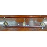 A 22" stained wood backed coat rack with three brass hooks