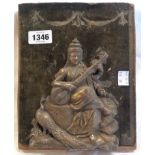 An old Indian white metal plaque, embossed with a seated deity playing a sitar, with a peacock
