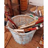 A wicker log basket containing assorted items including vintage and other tennis racket,
