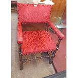 An early 20th Century oak framed elbow chair with studded red upholstery, set on turned supports