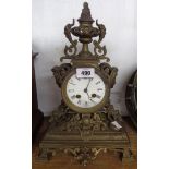 A late Victorian cast brass cased ornate mantel clock with urn to top and flanking masks with