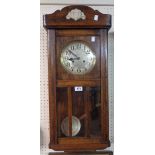 A 20th Century stained oak cased wall clock with visible pendulum and eight day gong striking