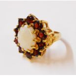A hallmarked 375 gold dress ring, set with large central milky opal within a ten stone garnet