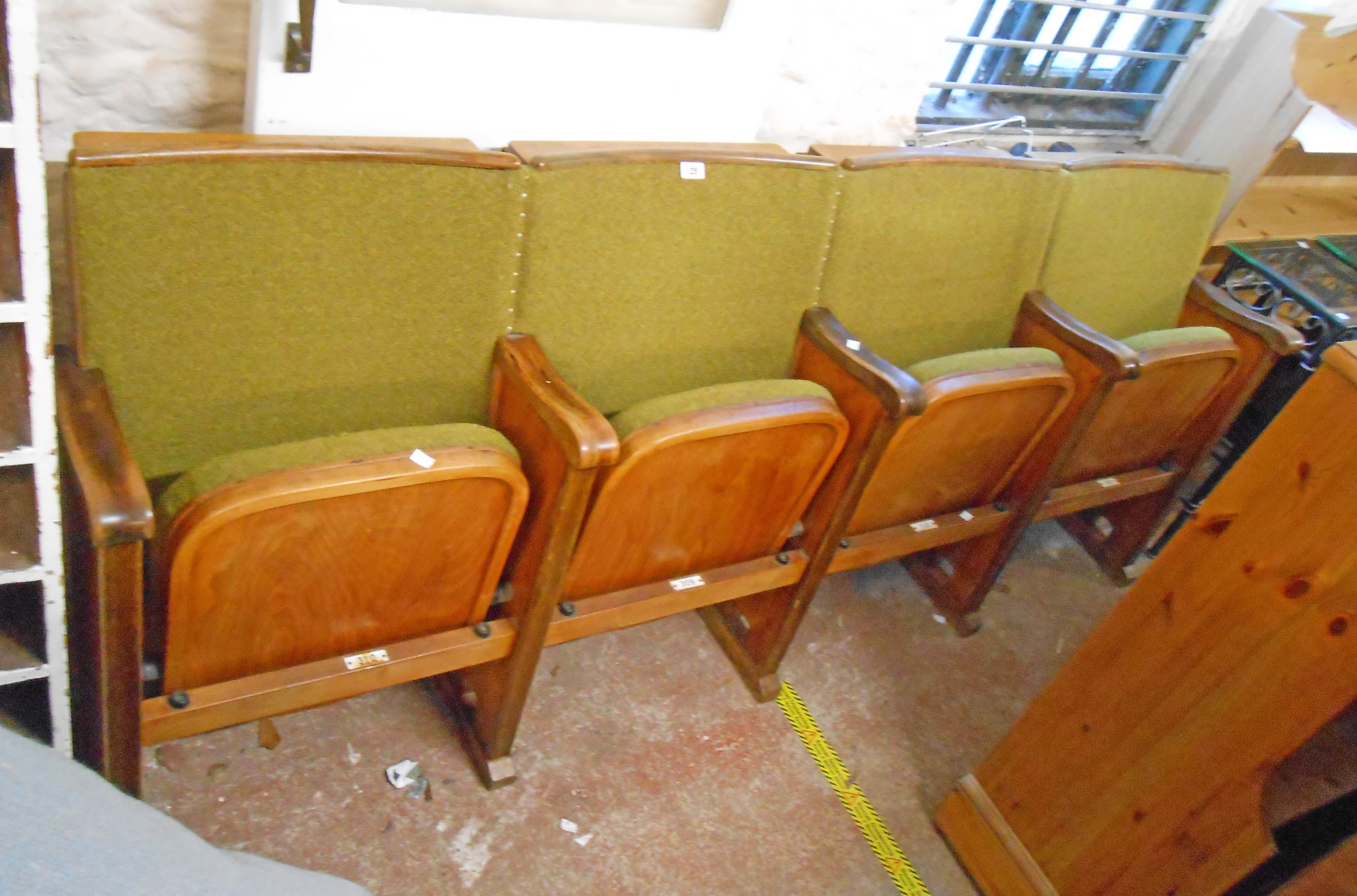 A row of four vintage cinema seats with polished wood part show frames, moulded arm rests and