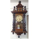 A stained walnut and mixed wood case wall clock with ornate pediment, flanking half columns and