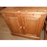 A 30" modern waxed pine cabinet enclosed by a pair of panelled doors, set on plinth base