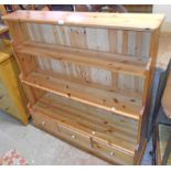 A 4' 2" polished pine three shelf waterfall open bookcase with three drawers under, set on plinth