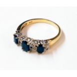 An import marked 375 gold ring, set with three dark sapphires interspersed with tiny diamonds