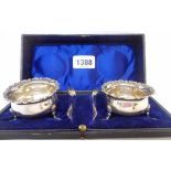 A late Victorian cased pair of silver salts with cast rims and lion paw feet and pair of spoons by