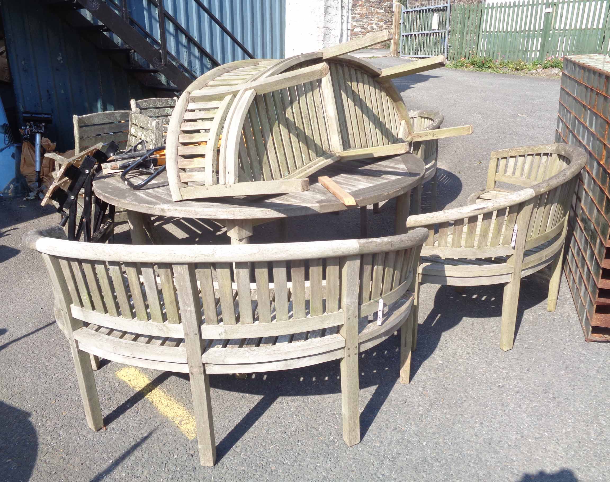 A teak patio set comprising large circular table and a set of four demi-lune bench seats