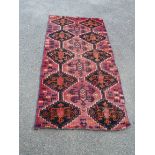 A faded wool rug with repeat gul motif on red ground - 1.88m X 84cm