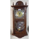 A 20th Century polished oak and mixed wood cased wall clock with visible pendulum, dial marked