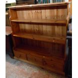 A 1.25m polished pine three shelf waterfall open bookcase with three drawers under, set on plinth