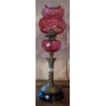 A Victorian table oil lamp with cranberry reservoir on spiral brass column, cranberry shade and