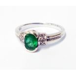 A hallmarked 375 white gold ring, set with central oval emerald and flanking tiny diamonds