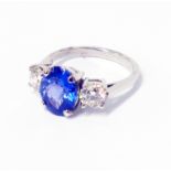 An unmarked white metal ring, set with central 2.82ct oval tanzanite flanked by two brilliant cut