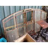 A pair of large metal industrial windows with arched tops - some panes missing