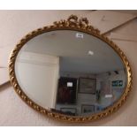 A reproduction gilt framed bevelled oval wall mirror with bow pediment