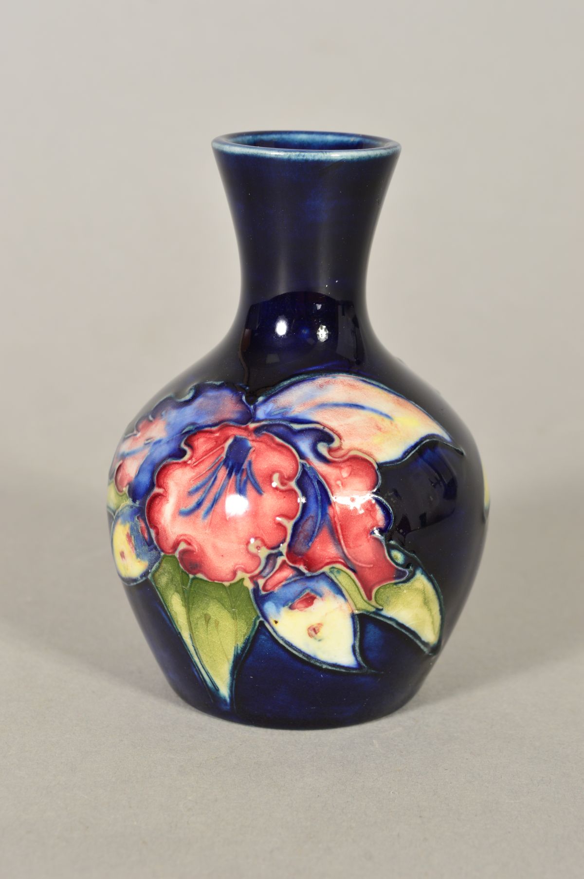 A SMALL MOORCROFT POTTERY BUD VASE, 'Orchid' pattern on blue ground, 'Queen Mary' label to base,