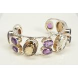 AN AMETHYST AND SMOKEY QUARTZ TORQUE BANGLE, of open design collet set with four diagonal oval