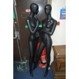 A PAIR OF BLACK GROUND FULL SIZED WOMAN SHOP DISPLAY MANNEQUINNS on circular glass stands