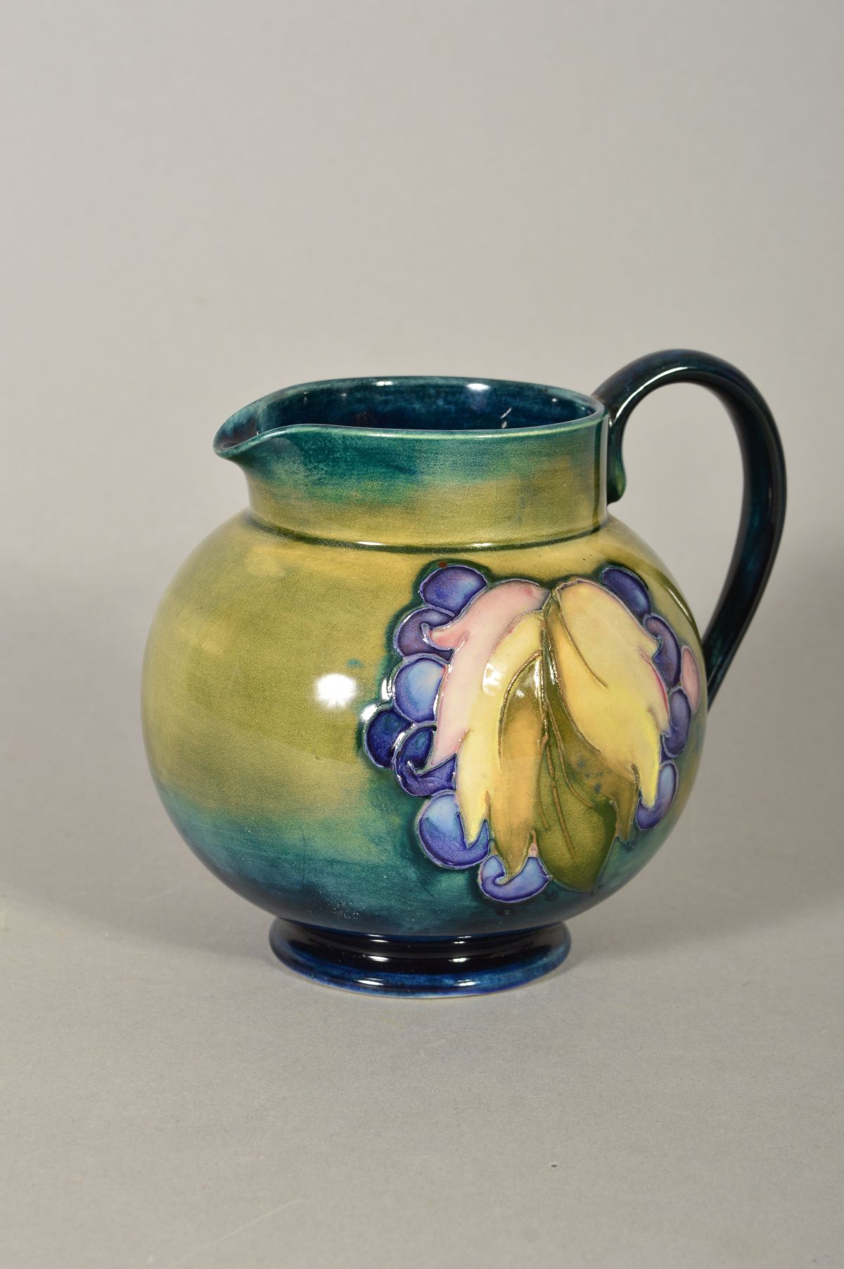 A WALTER MOORCROFT POTTERY FOOTED JUG, of bulbous form, leaf and berry pattern on green ground,