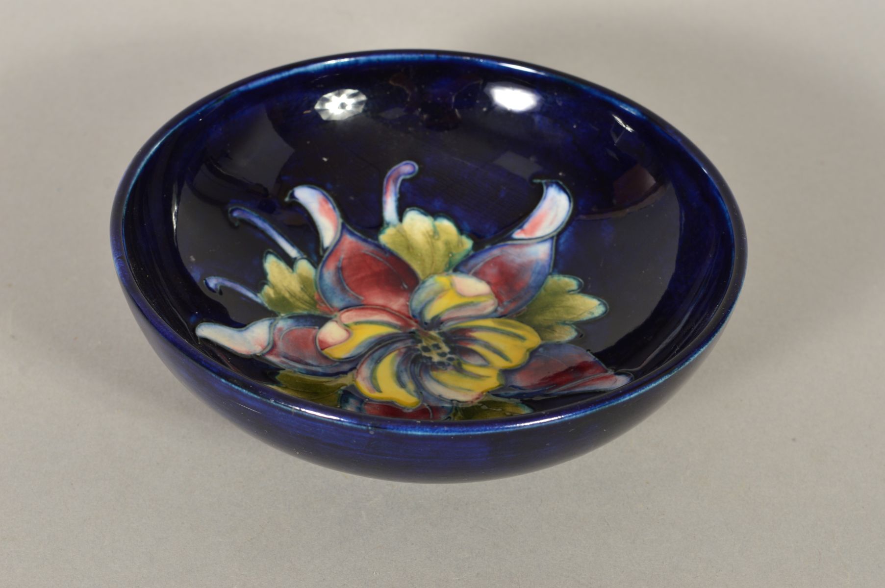 A SMALL MOORCROFT POTTERY FOOTED BOWL, 'Columbine' pattern on blue ground, impressed and painted