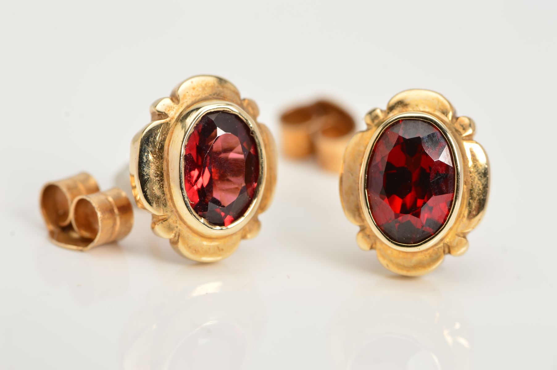 A PAIR OF GARNET STUD EARRINGS, each designed as an oval garnet in a collet setting within an