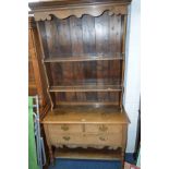 A LIGHT OAK DRESSER with a shaped apron and two shelves to the plate rack over two short and one