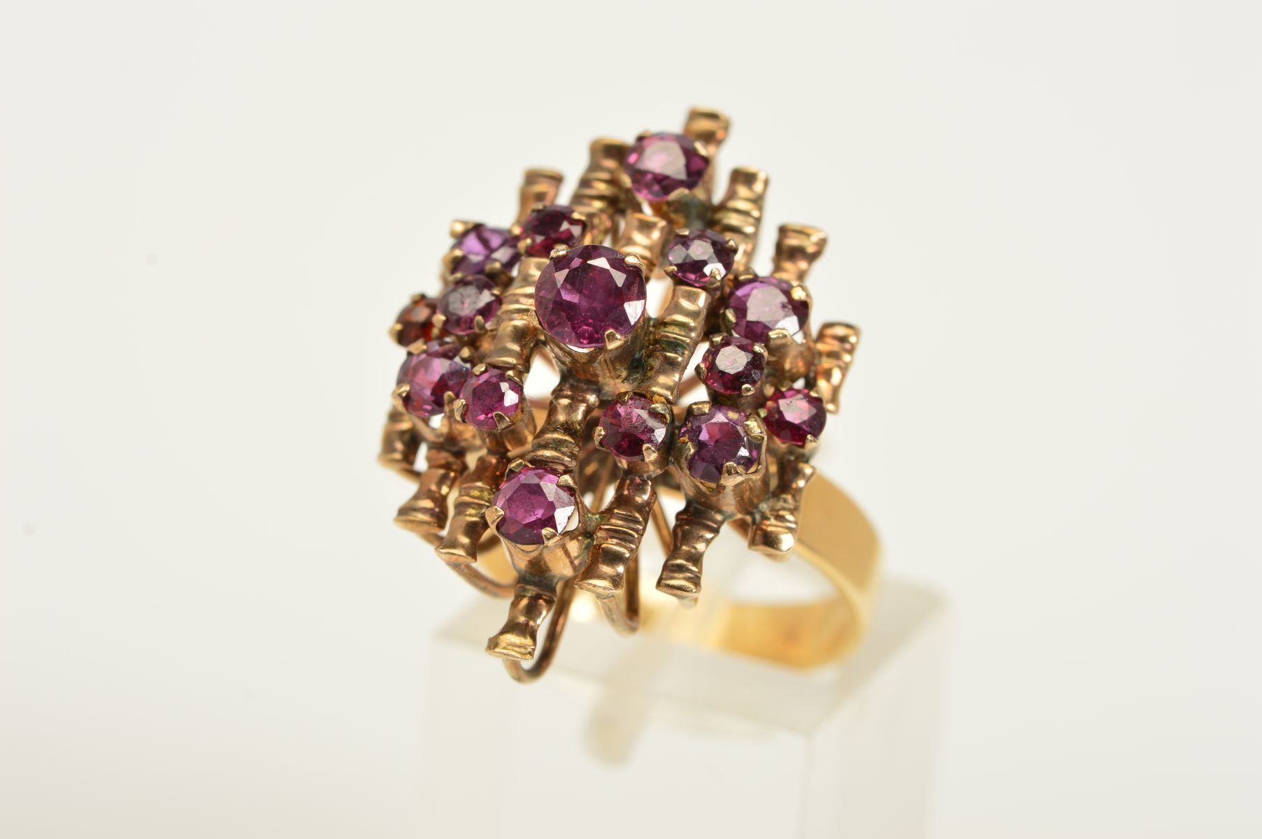 A GARNET DRESS RING, a tiered ring with open metal work set with fifteen circular garnets upon a