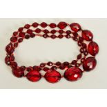 A FACETED RED PLASTIC BEAD NECKLACE, designed as a single row of graduated oval faceted red