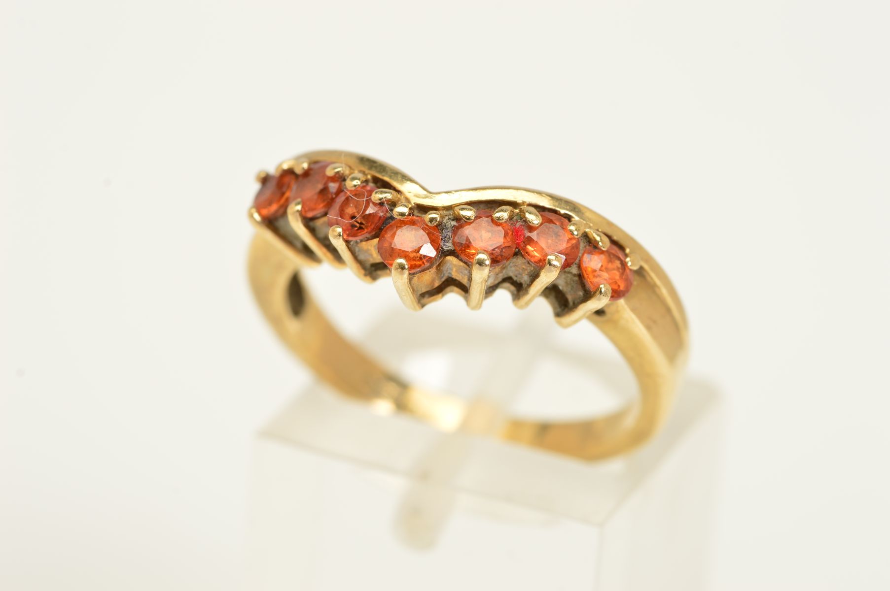 A 9CT GOLD GEM RING, the V-shape front set with a line of seven circular orange gems assessed as