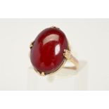 A CABOCHON RING, designed as an oval red plastic cabochon ring within a four claw setting, ring size