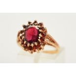 A 9CT GOLD GARNET RING, designed as a tiered cluster ring with a central oval cut garnet and