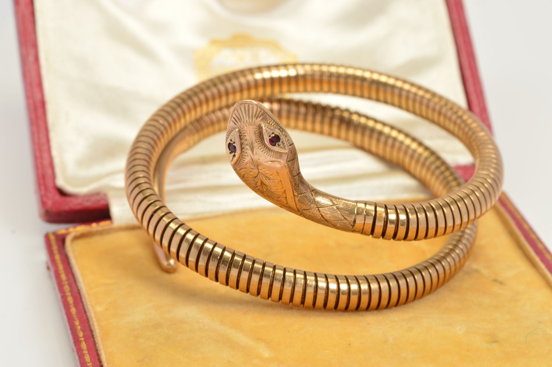 A COILED SNAKE BANGLE, of sprung design in a double coil, with red gem eyes, engraved decoration