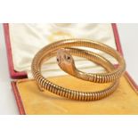 A COILED SNAKE BANGLE, of sprung design in a double coil, with red gem eyes, engraved decoration
