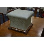A VICTORIAN UPHOLSTERED FOOTSTOOL over concave sides on a walnut base and ceramic casters, 50cm
