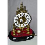 A BRASS SKELETON LOCK ON OVAL WOODEN PLINTH, white metal dial with Roman numerals has been re-