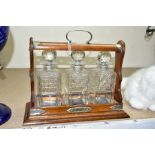 AN OAK TANTALUS, having EPNS handle and decoration holding three cut glass decanters (sd) (key)