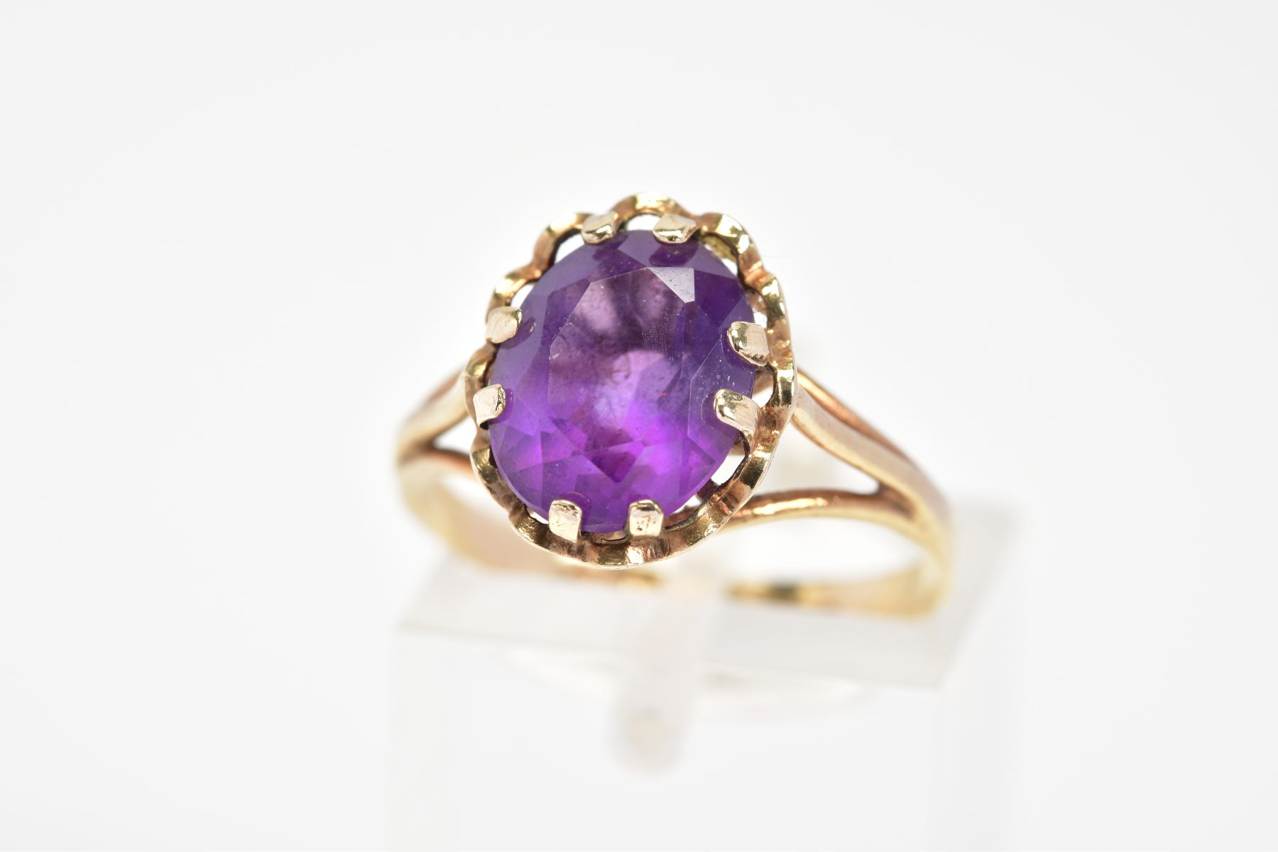 A 9CT GOLD AMETHYST RING, designed with a central oval cut amethyst within a scallop surround to the