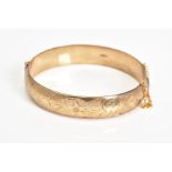 A MID TO LATE 20TH CENTURY 9CT GOLD OVAL BANGLE, half engraved in a floral and foliate design,