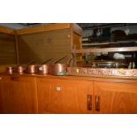A SET OF FIVE GRADUATING COPPER PANS with iron hooped handles and an oak wall rack (6)