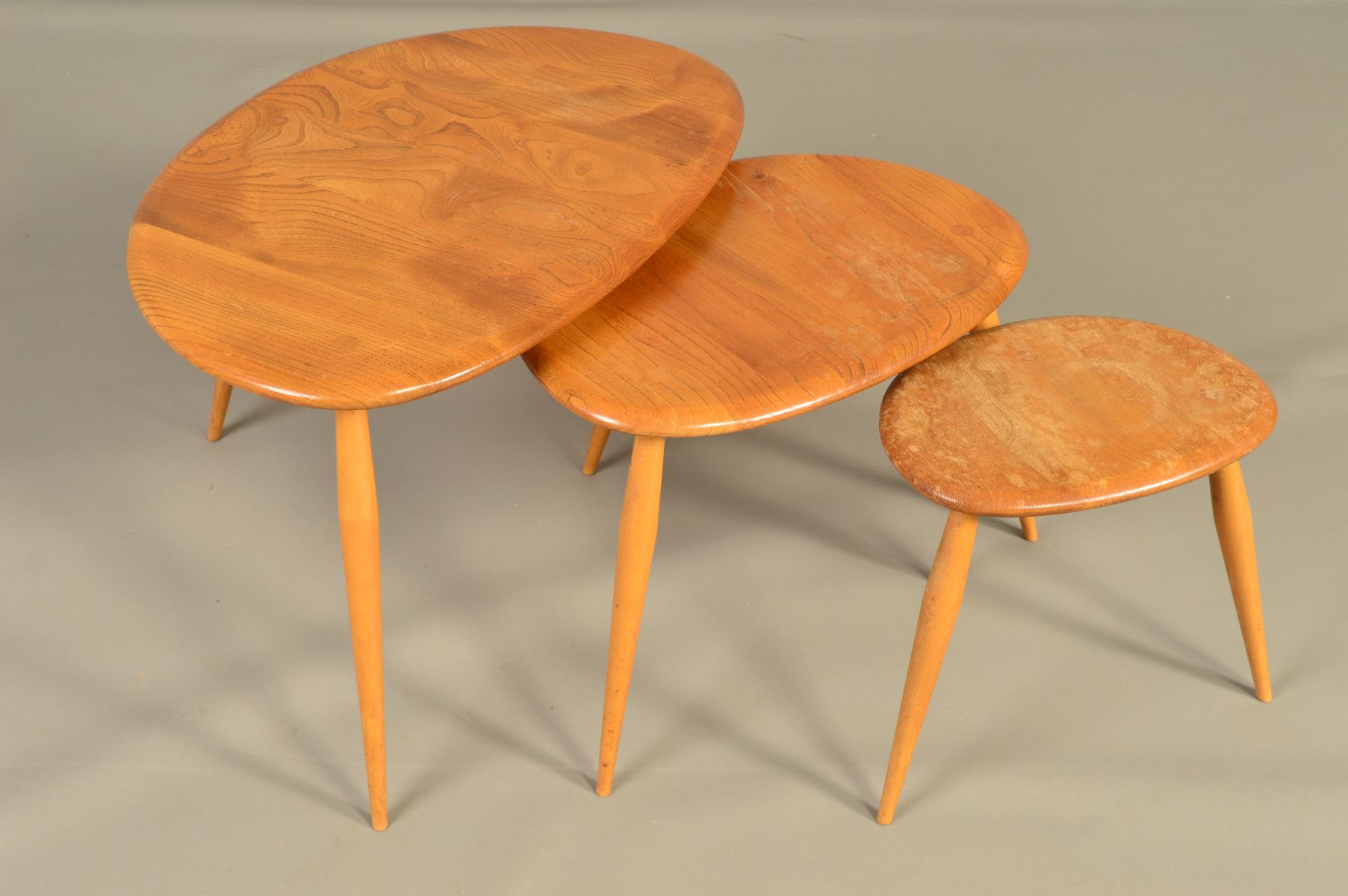 AN ERCOL BLONDE ELM PEBBLE NEST OF THREE TABLES, on triple beech cylindrical tapering legs,