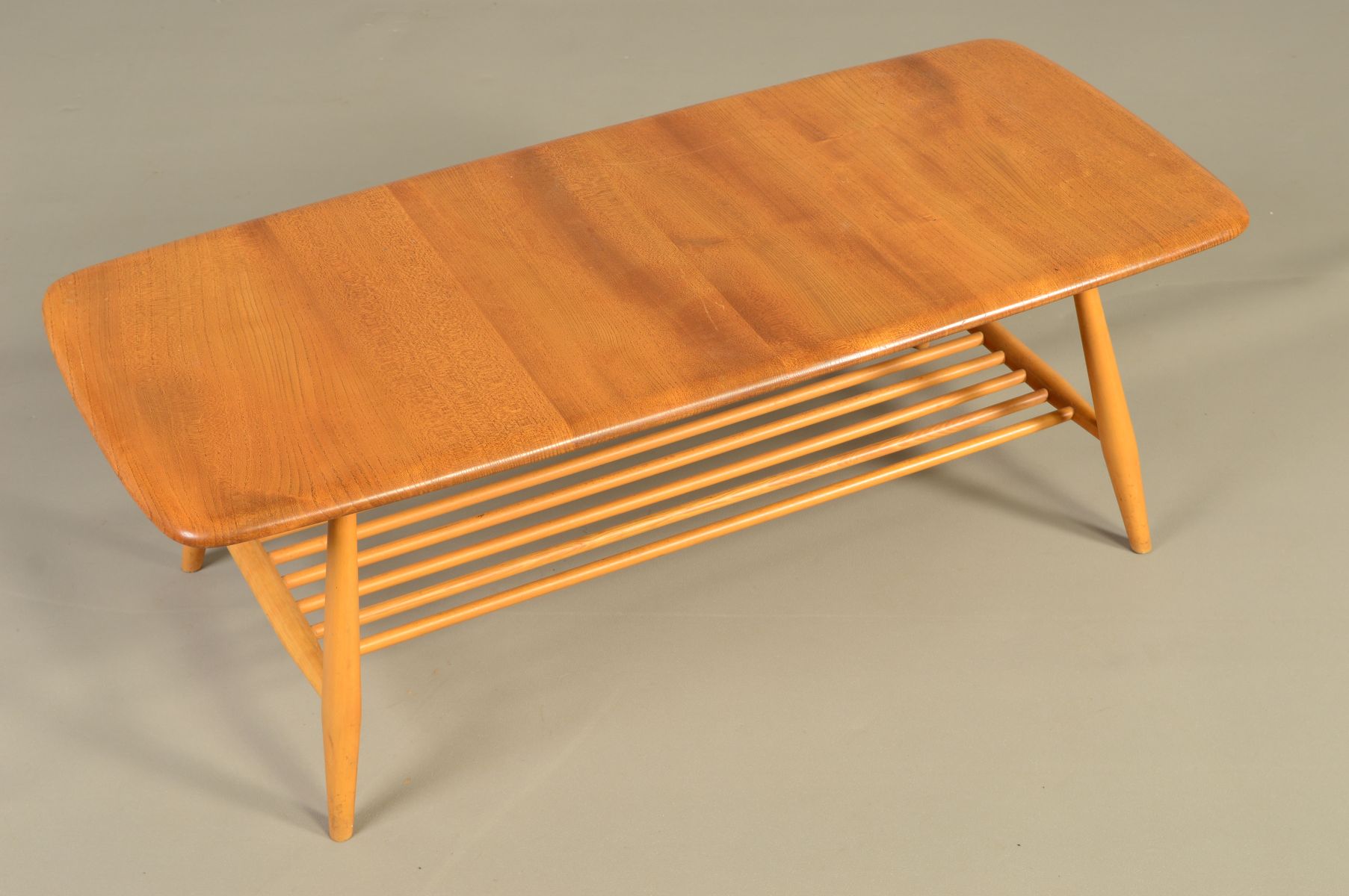 AN ERCOL BLONDE ELM RECTANGULAR COFFEE TABLE, on four beech tapering legs united by a spindled