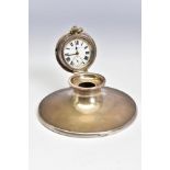 AN EDWARDIAN SILVER CAPSTAN INKWELL, the hinged cover fitted with a top wind pocket watch, the white