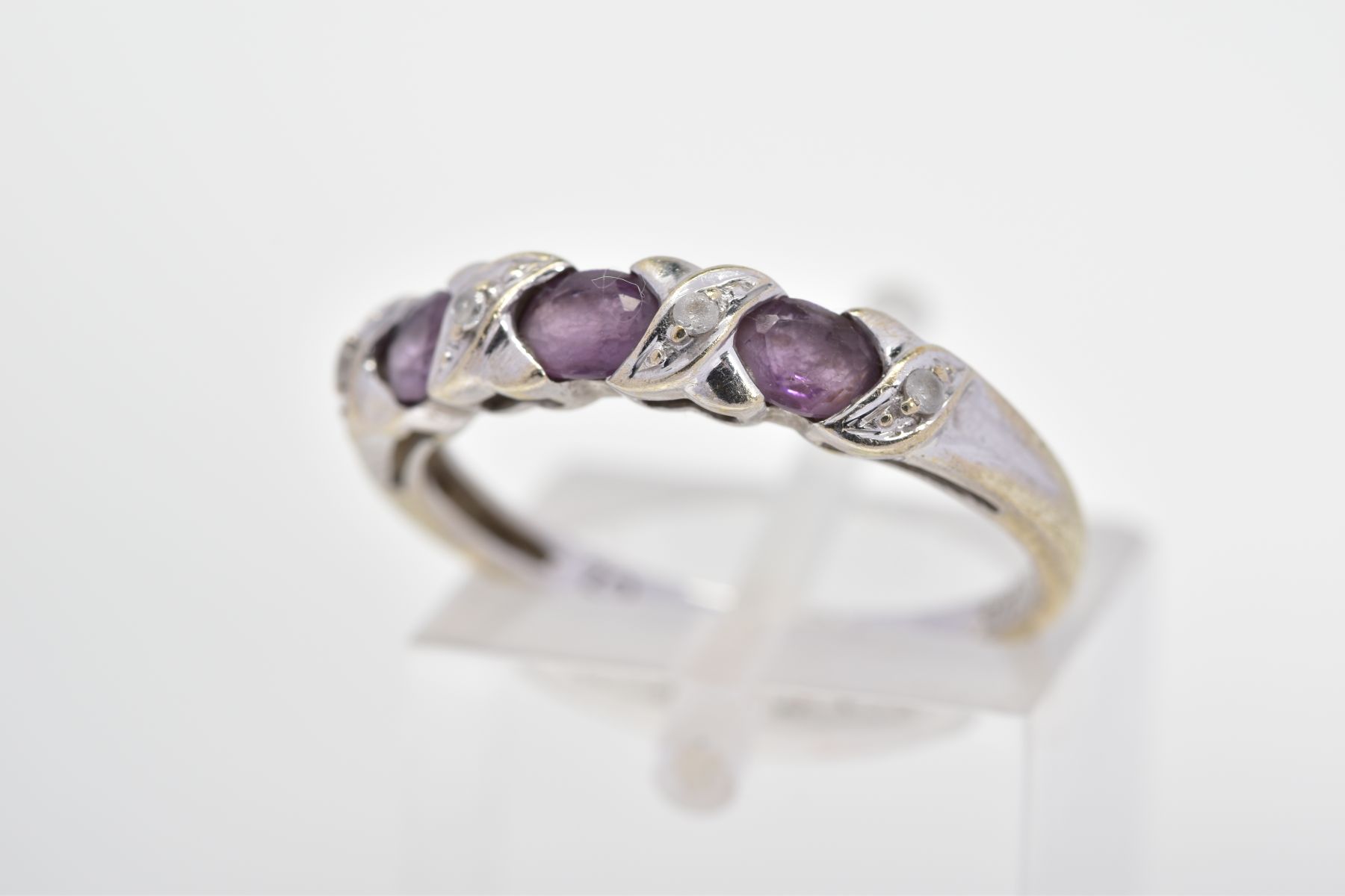 A CUBIC ZIRCONIA DRESS RING, designed as three oval purple cubic zirconias, each interspaced by a