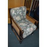 AN EARLY 20TH CENTURY OAK BERGERE ARMCHAIR with removable cushions