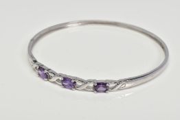 A CUBIC ZIRCONIA BANGLE, designed as three oval purple cubic zirconias interspaced by open cross